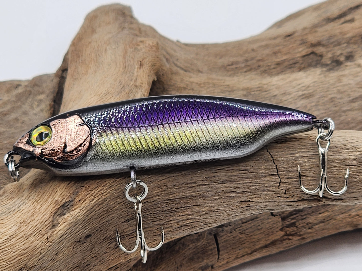 A collection of artificial fishing lures with realistic fish-like shapes and multiple colors, displayed on a piece of driftwood.