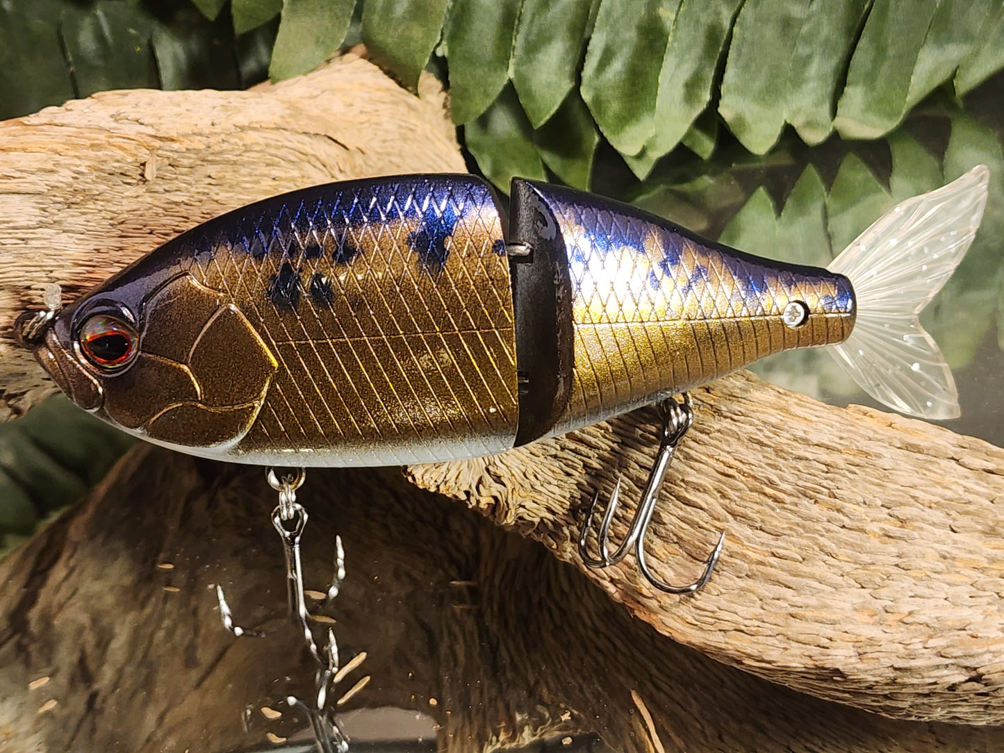 A realistic looking artificial fishing bait with silver and gold scales, and a detailed face, attached to a hook.