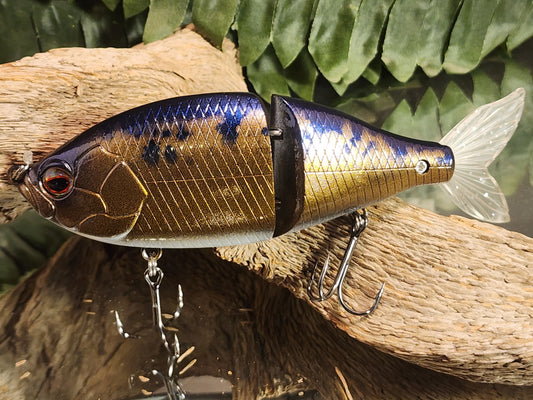 A realistic looking artificial fishing bait with silver and gold scales, and a detailed face, attached to a hook.