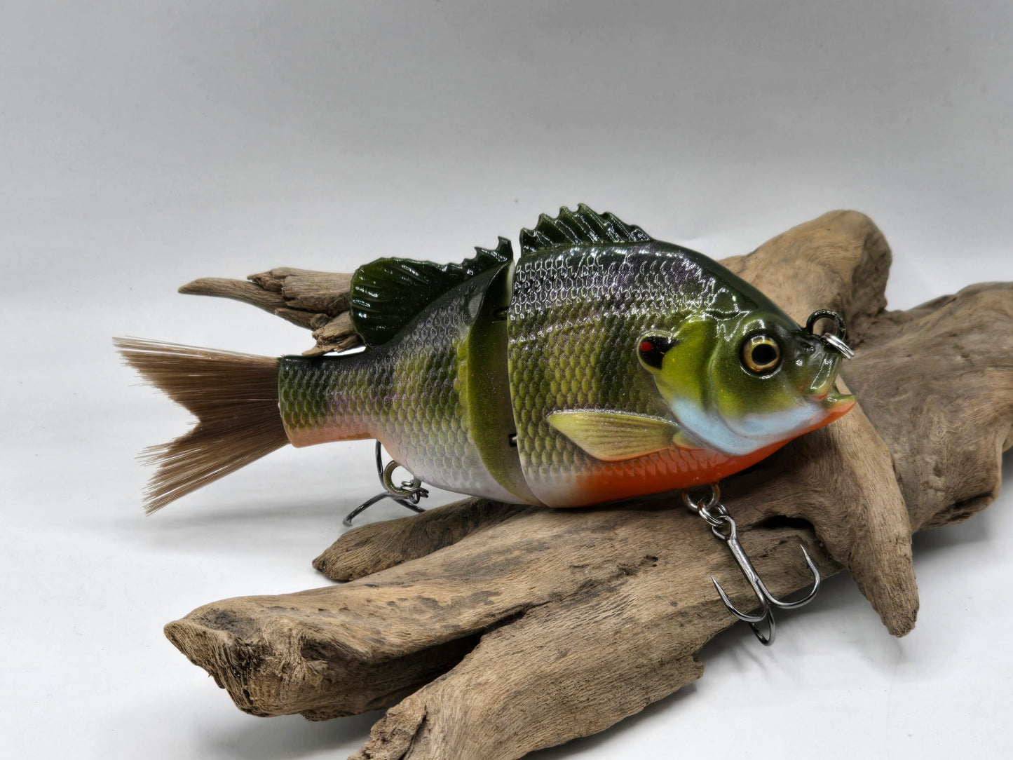 Fishing lure resembling a fish on a piece of driftwood against a white background
