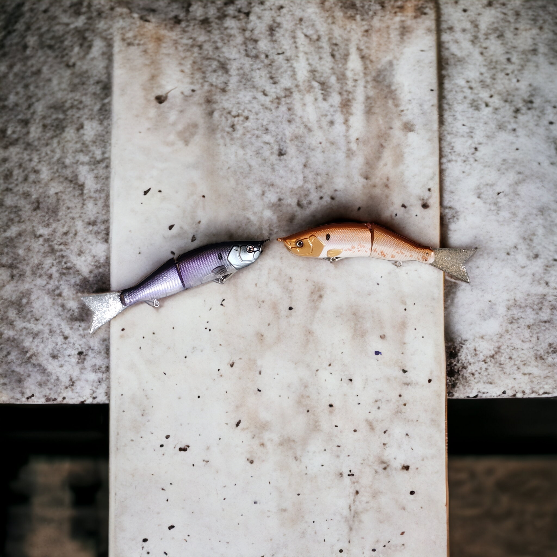 Two jointed glide baits designed for fishing, positioned on a concrete surface.