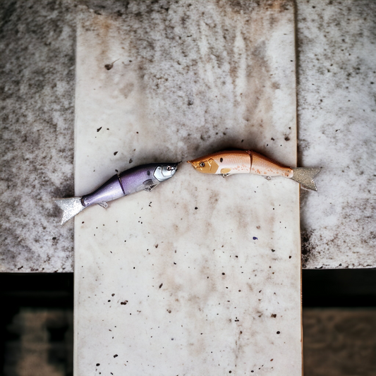 Two jointed glide baits designed for fishing, positioned on a concrete surface.