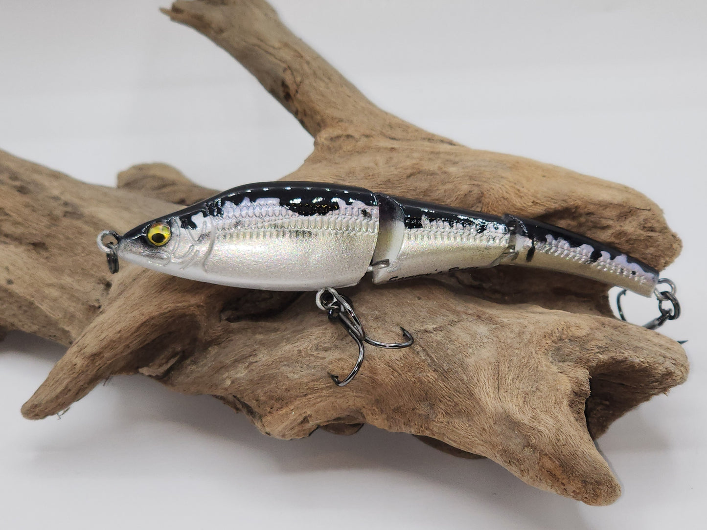 Custom painted fishing lure with silver, green, and pink colors, featuring black spots and realistic fish detailing, positioned on a wooden surface.